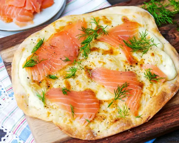 Flammkuchen mit Lachs, belegt mit zarten Lachsscheiben und frischem Dill, auf einem Holzbrett serviert.