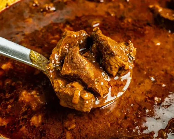 Ein Löffel voller herzhaftem Wildschweingulasch, bereit zum Servieren. Dieses Wildschweingulasch Rezept verspricht ein köstliches Gericht.