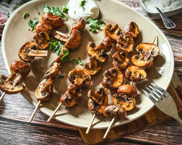Gegrillte Champignons am Spieß, mit Kräutern verfeinert, auf einem Teller serviert. Ein Genuss für jeden Pilzliebhaber!