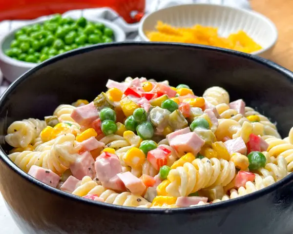 Ein cremiger nudelsalat mit mayonaise, garniert mit Erbsen, Mais, Paprika und Schinkenwürfeln.