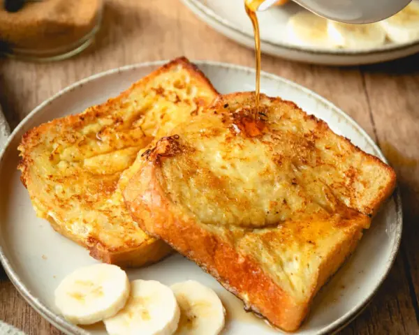 Armer Ritter, goldbraun gebraten, mit Sirup übergossen und Bananenscheiben garniert. Ein köstliches Frühstück!