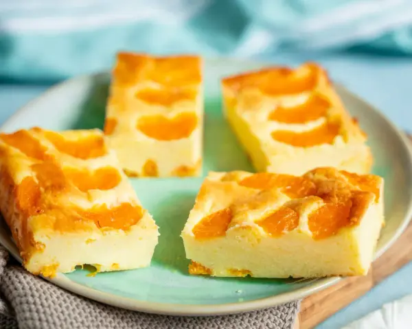 Vier Stücke saftiger Mandarinen Quark Kuchen auf einem Teller, garniert mit frischen Mandarinenstücken.