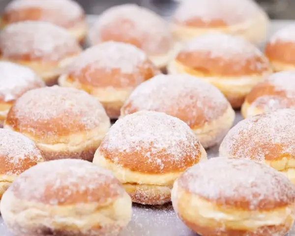 Eine Reihe von frisch gebackenen, mit Puderzucker bestäubten Berliner Pfannkuchen liegt auf einem Blech.