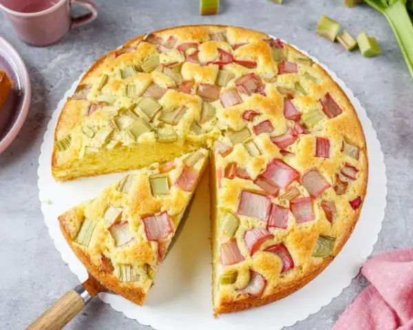Saftiger Rhabarberkuchen, ein Klassiker unter den Rezepten mit Rhabarber. Ein Stück wird gerade herausgehoben.