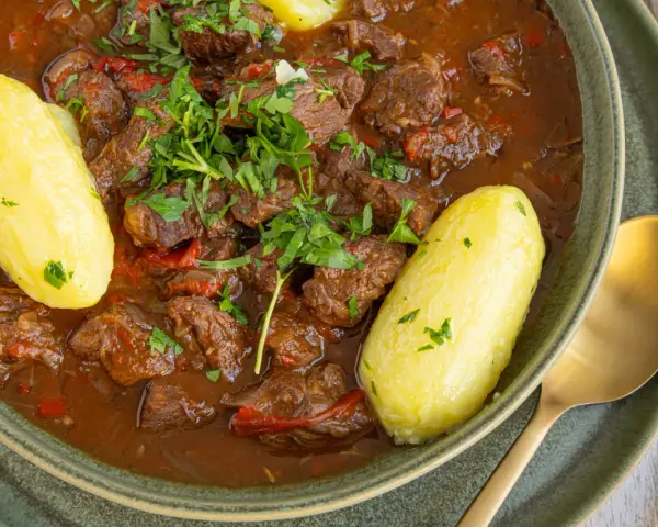 Herzhaftes Gulasch im Schnellkochtopf, serviert mit Salzkartoffeln und frischer Petersilie. Ein Klassiker, der schnell zubereitet ist.