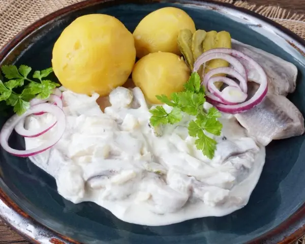 Marinierter Hering in cremiger Soße mit Salzkartoffeln, Gurken und Zwiebelringen. Ein deftiges Gericht, das Appetit macht.