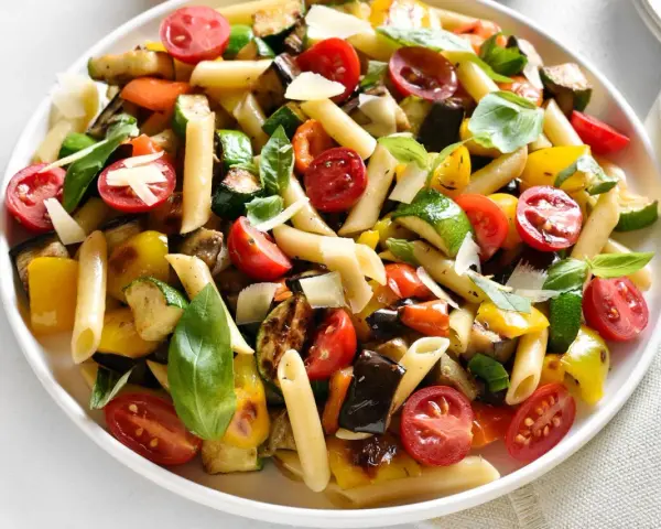 Bunter Nudelsalat ohne Mayo mit Penne, gegrilltem Gemüse, Kirschtomaten und Basilikum, garniert mit Parmesan.