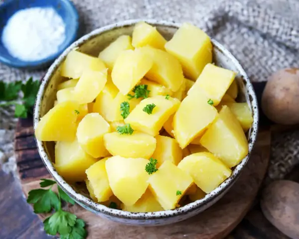 Schüssel mit dampfenden Salzkartoffeln, garniert mit Petersilie. Daneben eine kleine Schale mit Salz und rohe Kartoffeln.
