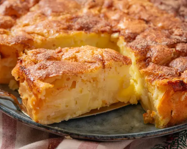 Ein Stück von einem goldbraunen, sehr feinen Apfelkuchen mit Zimt bestreut, wird mit einer Tortenheber herausgehoben.