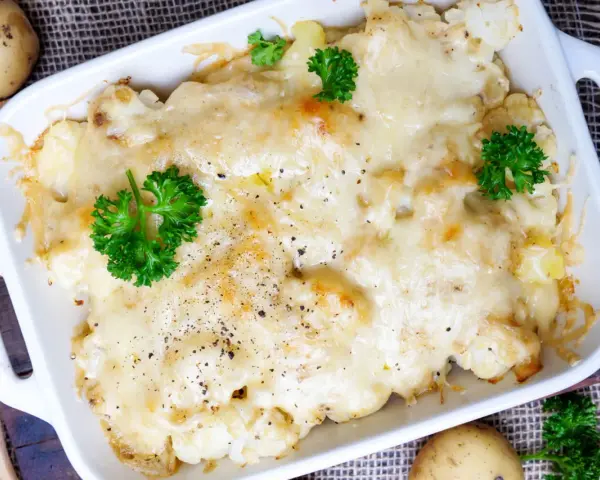 Herzhafter Blumenkohl Auflauf mit geschmolzenem Käse und frischer Petersilie, garniert mit Pfeffer.