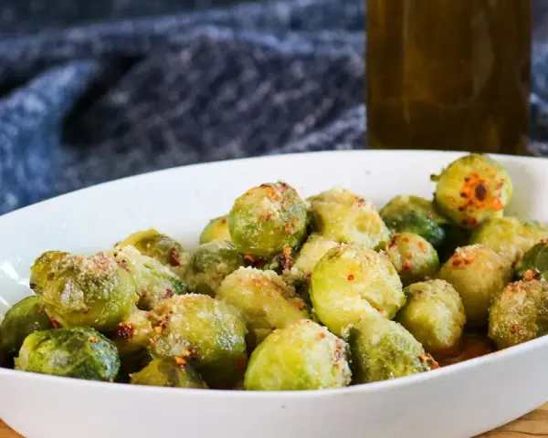 Ein weißes Ovalschälchen gefüllt mit knusprigem Rosenkohl, bestreut mit Parmesan und Chili-Flocken.