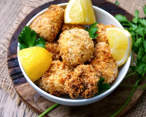 Knuspriger blumenkohl im airfryer, goldbraun paniert, serviert mit frischen Zitronenspalten und Petersilie.