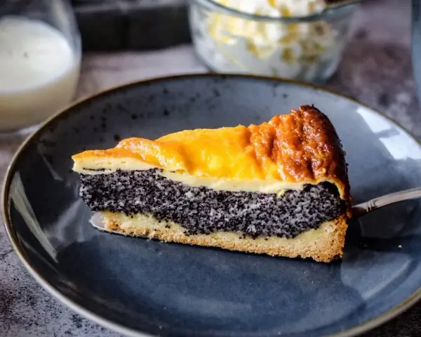 Ein saftiges Stück Mohnkuchen mit Pudding-Schicht auf einem blauen Teller, bereit zum Genuss.