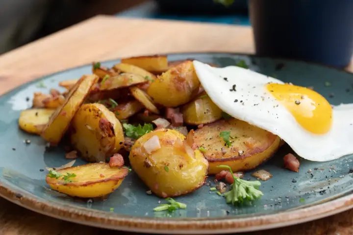 Bratkartoffeln mit Speck und einem Spiegelei, ein klassisches Rezept für ein herzhaftes Frühstück oder Abendessen.