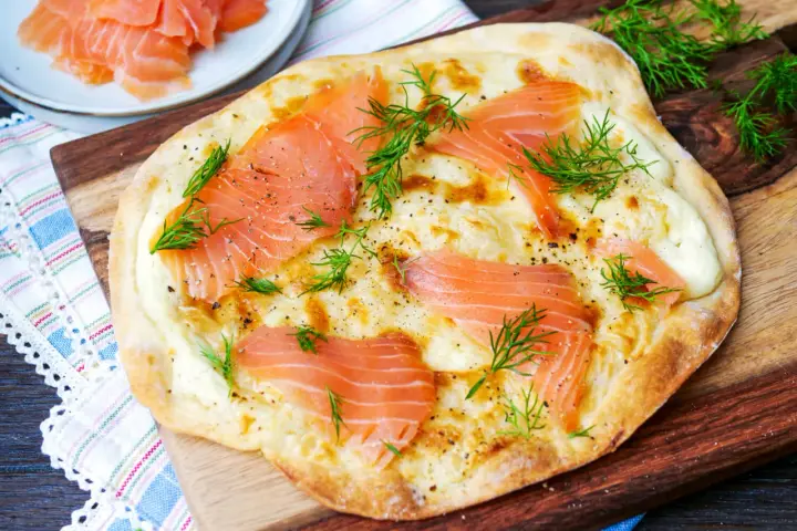 Flammkuchen mit Lachs, belegt mit zarten Lachsscheiben und frischem Dill, auf einem Holzbrett serviert.