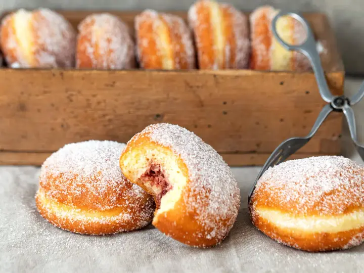 Zuckerüberzogene Berliner, eines davon mit Marmeladenfüllung, warten auf das nächste berliner rezept.