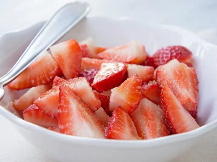 Schüssel mit marinierten Erdbeeren, die mit einem Löffel serviert werden. Saftige, rote Erdbeerstücke glänzen im Licht.