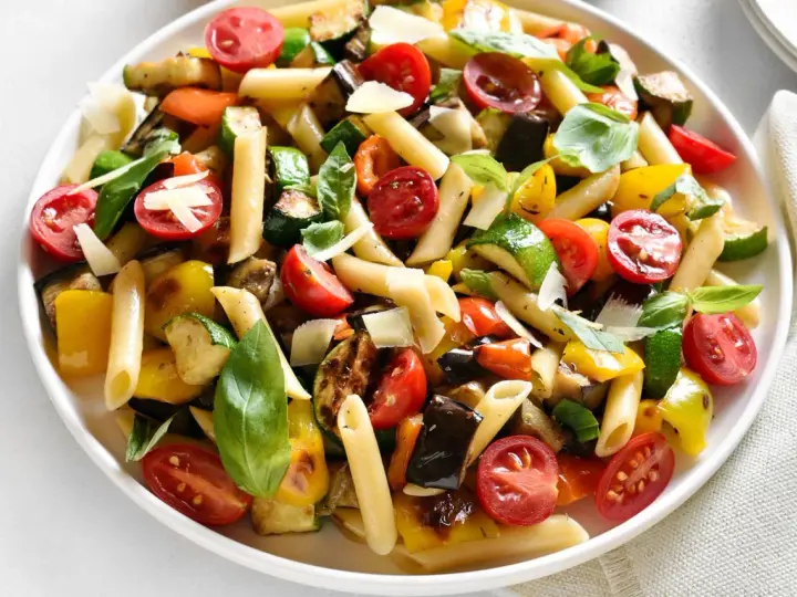 Bunter Nudelsalat ohne Mayo mit Penne, gegrilltem Gemüse, Kirschtomaten und Basilikum, garniert mit Parmesan.