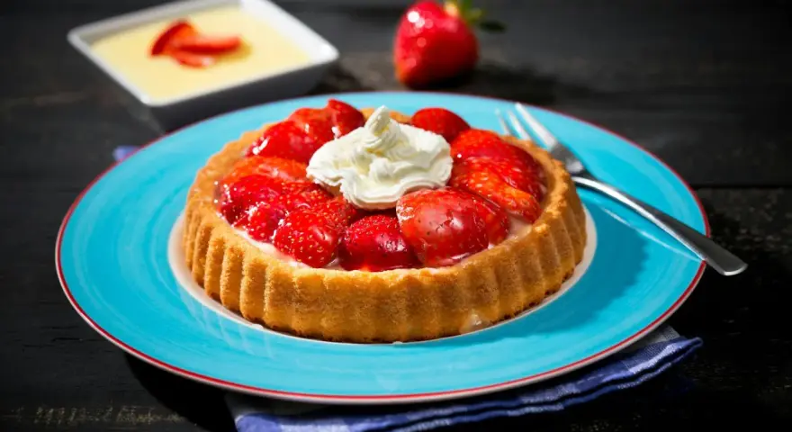 Erdbeerkuchen mit fertigboden, belegt mit frischen Erdbeeren und Sahne, auf einem blauen Teller.