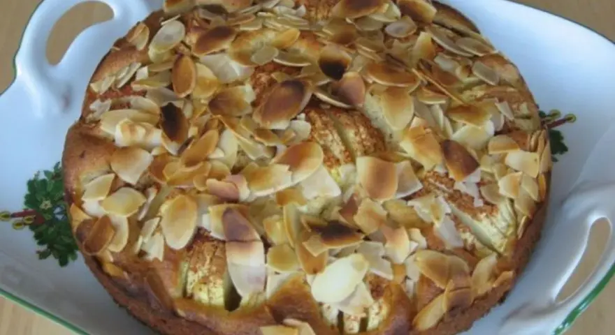 Ein köstlicher, kleiner Apfelkuchen mit gerösteten Mandelblättchen auf einer verzierten Servierplatte.