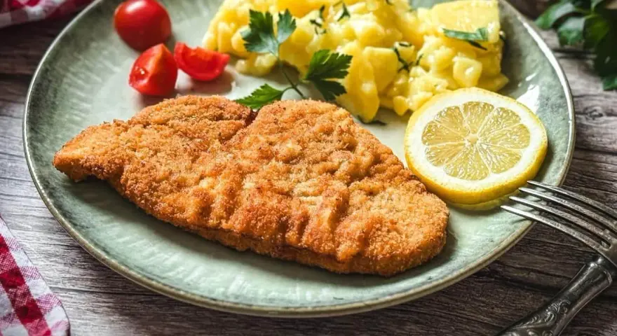 Perfekt gebratenes Putenschnitzel mit Kartoffelsalat, Tomaten und Zitrone auf einem Teller.