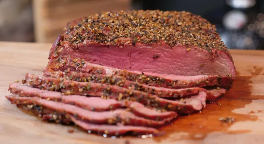 Perfekt gegarter Roastbeef Braten, saftig und rosa, mit einer würzigen Kruste aus Pfeffer und Kräutern, auf einem Holzbrett.