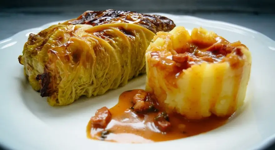 Ein goldbraunes Kohlrouladen-Rezept auf einem Teller, serviert mit Kartoffelpüree und einer herzhaften Sauce.