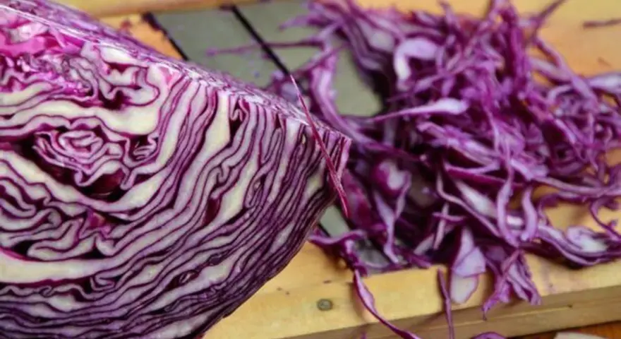 Ein halber Rotkohl liegt auf einem Holzbrett, daneben fein geschnittener Rotkohl für einen Salat.