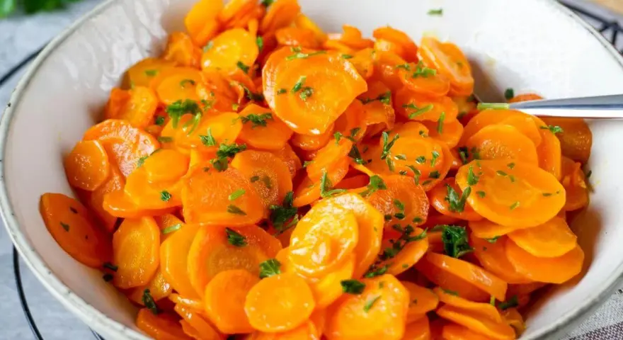 Schüssel mit glasierten Karottenscheiben, garniert mit Petersilie. Perfekt gekochte Karotten, die Lust auf mehr machen.