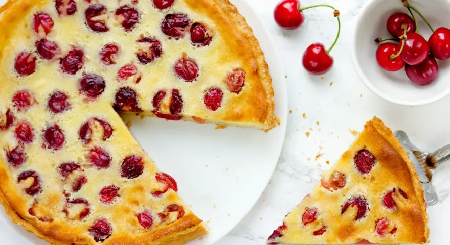 Ein köstlicher Pudding Kirsch Kuchen, mit frischen Kirschen belegt und goldbraun gebacken. Ein Stück wird gerade serviert.