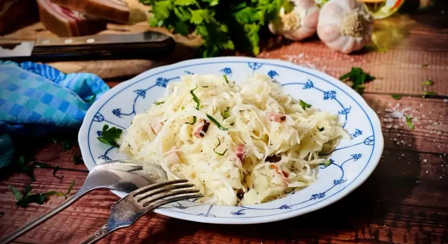 Ein Teller mit Krautsalat, garniert mit Petersilie. Daneben liegen Gabel und Löffel. Ein leckeres Krautsalat Rezept für dich!