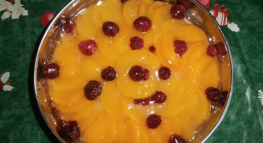 Fruchtiger Tortenboden ohne Ei, belegt mit Pfirsichspalten und Himbeeren in Gelee.