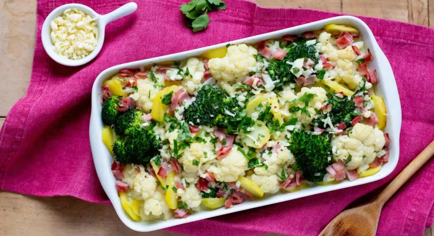 Ein herzhafter Blumenkohl-Brokkoli-Auflauf mit Kartoffeln und Schinken, bestreut mit frischer Petersilie und Käse.