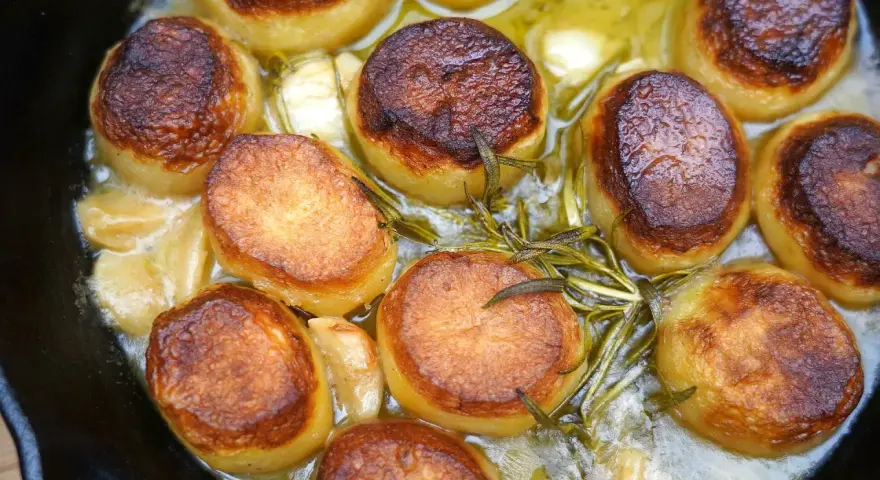 Saftige Fondant Kartoffeln mit Rosmarin und Knoblauch in einer Gusseisenpfanne, goldbraun gebraten.