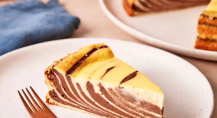 Ein Stück Zebrakuchen mit Quark, das auf einem Teller liegt, daneben eine Gabel.