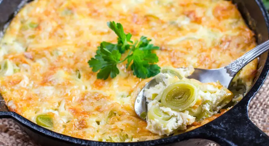 Ein goldbraunes Kartoffel-Lauch-Gratin in einer Gusseisenpfanne, mit einem Löffel herausgenommen, garniert mit Petersilie.