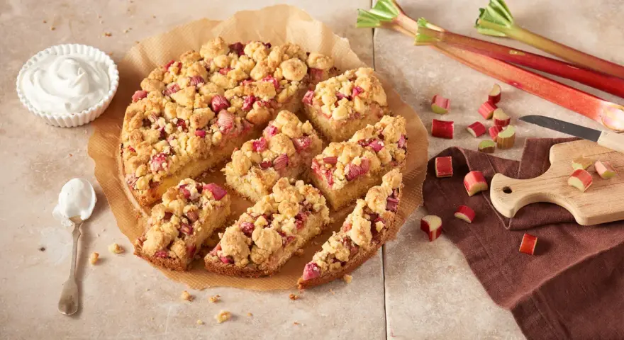 Ein saftiger Rhabarberkuchen mit Streuseln, perfekt für ein Rhabarberkuchen Rezept. Dazu eine Schüssel Schlagsahne.