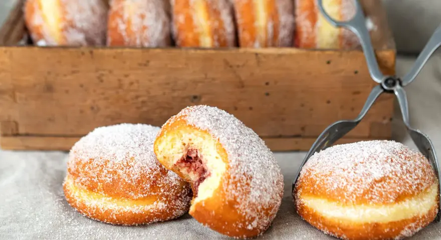 Zuckerüberzogene Berliner, eines davon mit Marmeladenfüllung, warten auf das nächste berliner rezept.