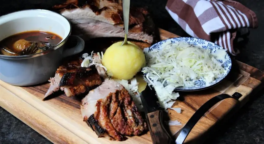 Deftige dicke Rippe mit Klößen, Sauerkraut und dunkler Soße auf Holzbrett.