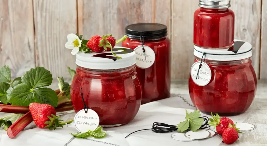 Gläser mit Erdbeer-Rhabarber-Marmelade, garniert mit frischen Erdbeeren und Blüten.