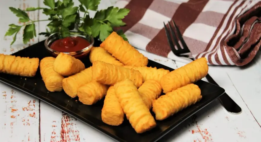 Goldbraune Kroketten, frisch zubereitet, liegen auf einem schwarzen Teller. Dazu gibt es Ketchup und frische Petersilie. Perfekt, um Kroketten selber machen zu lernen!