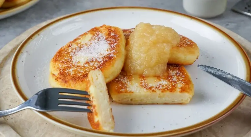 Goldbraune Quarkkeulchen, bestreut mit Puderzucker, serviert mit Apfelmus. Ein köstliches Quarkkeulchen Rezept zum Genießen.