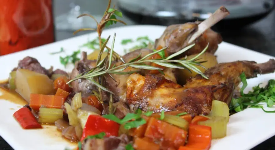 Klassisches Kaninchen-Rezept: Zartes Kaninchen mit Wurzelgemüse und Rosmarin auf einem weißen Teller serviert.
