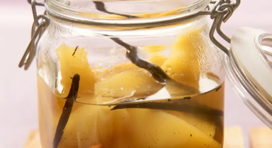 Ein Glas mit Quittenkompott, verfeinert mit Vanilleschoten. Die Fruchtstücke schimmern golden im Sirup.
