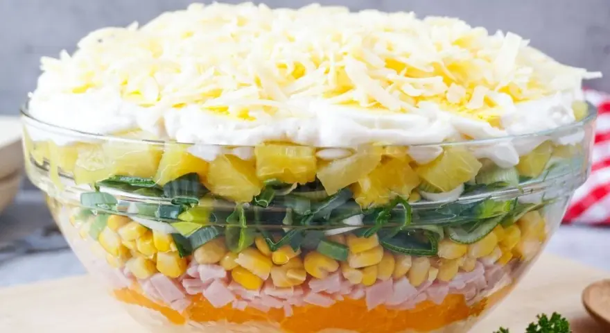 Schichtsalat rezept: Ein bunter Schichtsalat in einer Glasschüssel mit Ananas, Lauch, Mais, Schinken, Orange, Ei und Käse.