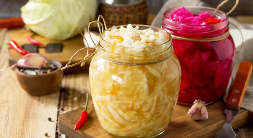 Zwei Gläser mit selbstgemachtem Sauerkraut und Rotkohl, daneben frischer Kohl, Knoblauch und Chilis.