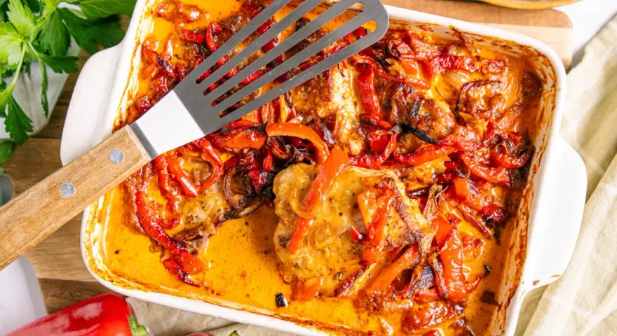 Herzhaftes Paprika Sahne Schnitzel in einer Auflaufform, mit roten Paprikastreifen und Zwiebeln in cremiger Sauce.