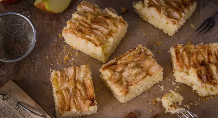 Saftige Apfel-Blechkuchen-Rezepte, bestreut mit Zimt. Ein Stück wird gerade mit einer Gabel probiert.
