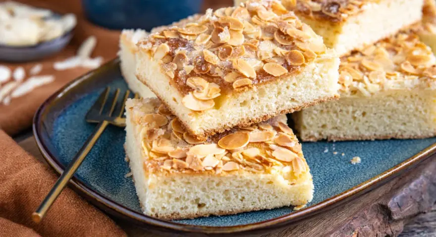 Original norddeutscher Butterkuchen mit Mandeln und Zucker bestreut, auf einem blauen Teller angerichtet.