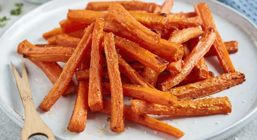 Knusprige karotten pommes, goldbraun gebacken, liegen auf einem Teller. Ein kleines Holzgabelchen liegt daneben.